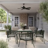 Patio exterior con cadeiras verdes SEGERÖN, mesa rectangular e vaso branco. Ventilador de teito, casa branca e muro de ladrillo.