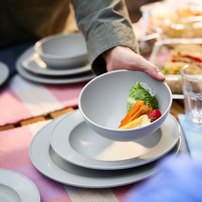 Cunca gris Sgrabba chea de verduras en pratos apilados, suxeitada por unha man.
