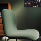Cadeira tapizada verde menta moderna, ben acolchada, con base metálica elegante contra a parede verde.