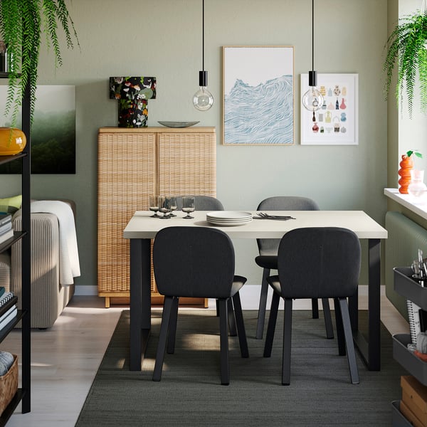 Un comedor moderno con mesa SKÅLSTA , cadeiras grises, decoracións brancas, fotos, luces e unha alfombra verde. Minimalista e acolledor.