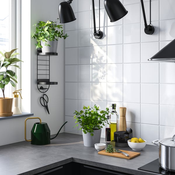 Cociña moderna con soporte de plantas verdes, plantas en pota, baldosas brancas, mostrador escuro, estufa de aceiro, lámpadas negras, limóns, herbas, ferramentas.