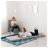 Dous nenos descansan nunha habitación minimalista. Un le nun colchón modular gris, outro desprácese nun teléfono intelixente mentres se deita noutro colchón dobrado.