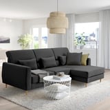 Sala de estar moderna: sofá seccional SLATORP gris escuro, pernas de madeira, mesa de café branca, lámpada de bambú, xanela grande, plantas, vestidos, libros.
