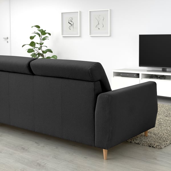 Sofá SLATORP negro moderno. Ancho, acolledor con costas altas. Contra a parede branca, deseño minimalista. Máis grande que a planta, máis pequena que a televisión.