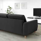 Sofá SLATORP negro moderno. Ancho, acolledor con costas altas. Contra a parede branca, deseño minimalista. Máis grande que a planta, máis pequena que a televisión.
