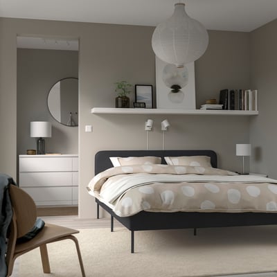 Dormitorio moderno con cama SLATTUM, roupa de cama de puntos, alfombra, cadeira, luz pendente, armario, paredes grises.