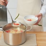 A persoa bota a sopa nunha cunca usando unha gran culler metálica cun mango de madeira.