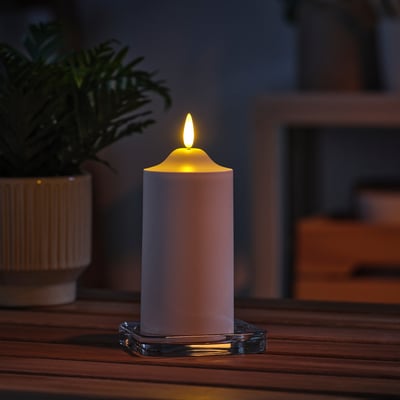 Ikea SMÅLOM candea led branca sobre soporte de vidro, brillando calorosamente sobre a mesa de madeira xunto á planta verde.