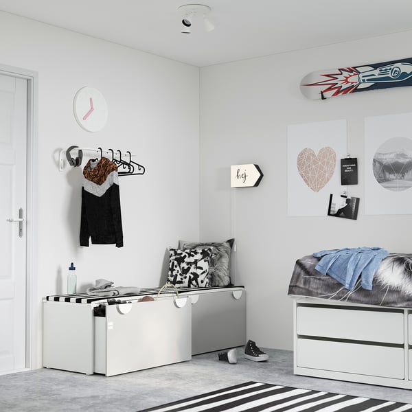 Dormitorio moderno con almacenamento branco SMÅSTAD e banco, alfombra a raias, reloxo de parede, carteis decorativos, auriculares e roupa en colgantes.