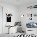 Dormitorio moderno con almacenamento branco SMÅSTAD e banco, alfombra a raias, reloxo de parede, carteis decorativos, auriculares e roupa en colgantes.