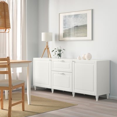 Sideboard branco SMEVIKEN con caixóns, lámpada, planta, vasos, baixo arte costeira.