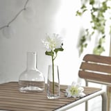 Mesa exterior con dalia branca SMYCKA en vaso de vidro transparente, realista e feita de plástico reciclado.