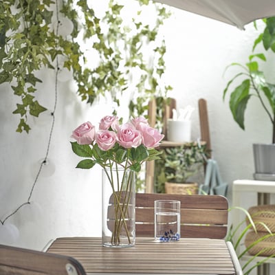 Vaso de rosas rosas sobre a mesa. Rodeada de plantas, ambiente ao aire libre.