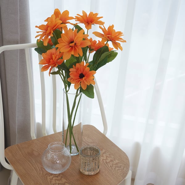 Vaso con flores laranxas sobre a mesa de madeira xunto á fiestra.