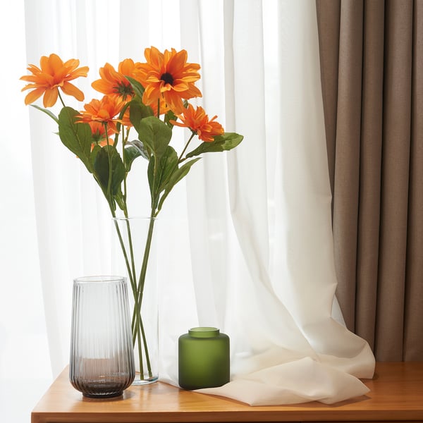 Vaso con flores laranxas preto da xanela, fondo de cortina, vela verde no estante de madeira.