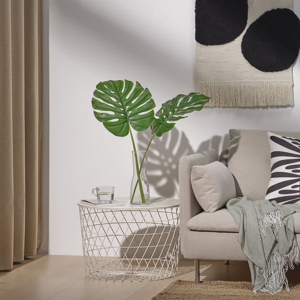 Salón moderno con folla verde en vaso, cadeira, manta, cortinas, arte de parede, chan de madeira e cunca de té.