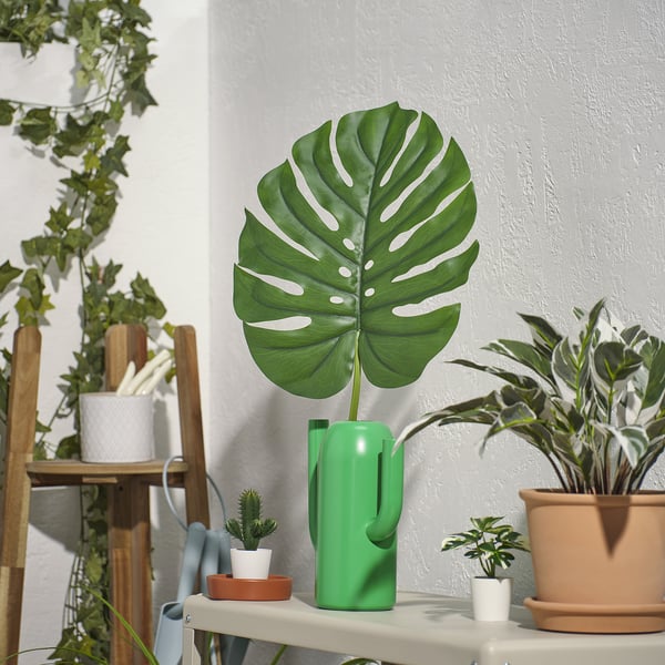 Vaso con folla verde grande, máis alto que outros, materiais reciclados.