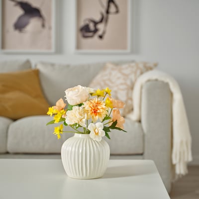 Vaso branco de costelas SMYCKA con flores sobre unha mesa nun acolledor salón.