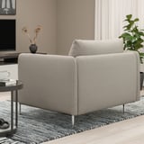 Sofá gris claro con coxíns de peluche e altas patas metálicas. Mesa lateral con cunca de café e libro.