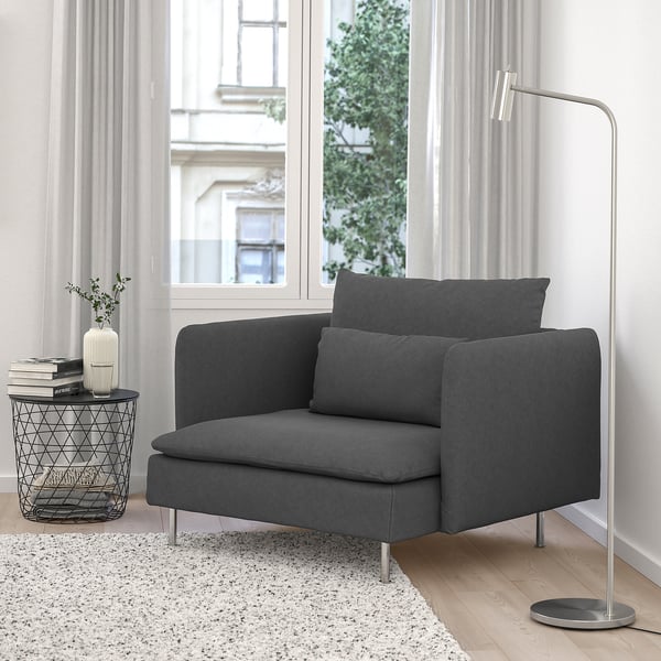 Sala de estar minimalista moderna con gran cadeira de brazos gris SÖDERHAMN, mesa lateral metálica, libros, vaso, lámpada e gran xanela.