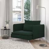 Acolledora cadeira verde SÖDERHAMN por fiestra. Asentos modernos e profundos, patas metálicas. Mesa final ordenada con libros e un vaso. Alfombra suave debaixo. Lámpada de chan á dereita.