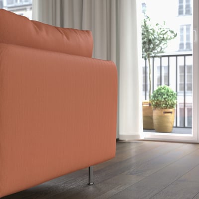 Unha cómoda chaise longue laranxa xunto a unha gran xanela con plantas, mostrando o seu asento relaxado e o seu deseño moderno.