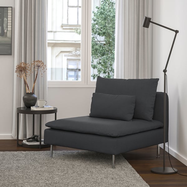 Cadeira SÖDERHAMN en gris escuro, elegante e baixo, situada preto dunha gran xanela con cortinas, xunto a unha pequena mesa redonda con flores secas e unha lámpada de chan.