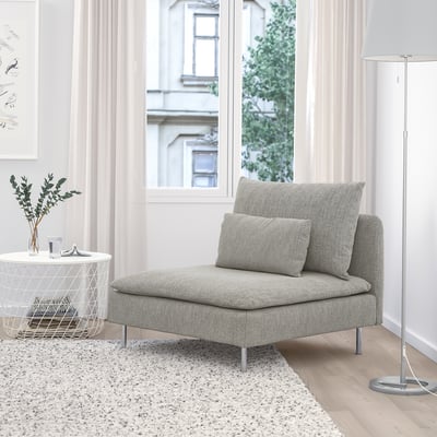 Cadeira gris SÖDERHAMN, baixa e suave con téxtil de elite. Pequena mesa lateral, lámpada de chan e arte nas proximidades. A gran fiestra amosa un edificio.