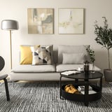 Sala de estar moderna con sofá SÖDERHAMN, branco con almofadas con patróns, mesa de café redonda negra, lámpada de chan e arte abstracta nas paredes.