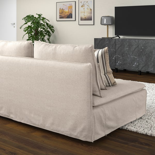 Sofá beige moderno SÖDERHAMN con almofada de raias, chan de madeira, alfombra branca, soporte de televisión, lámpada e arte da parede.