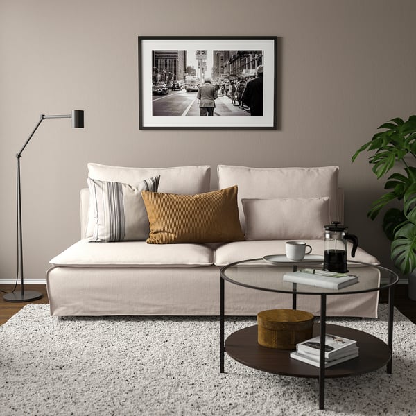 Sala de estar moderna con sofá SÖDERHAMN beige, coxíns, lámpada negra, mesa de café de vidro e planta verde.
