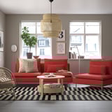 Sala de estar moderna con sofá vermello, alfombra, mesa de café, fiestras de vista á cidade e luz colgante.