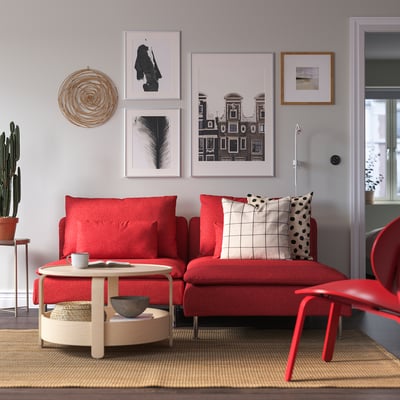 Sofá seccional vermello SÖDERHAMN con almofadas, alfombra beige, parede de galería, mesa de café con cunca e cunca.