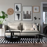 Sala de estar moderna con sofá SÖDERHAMN branco, coxíns grises, mesa de café negra, alfombra a raias e parede de galería. O sofá encaixa ben cos elementos circundantes.
