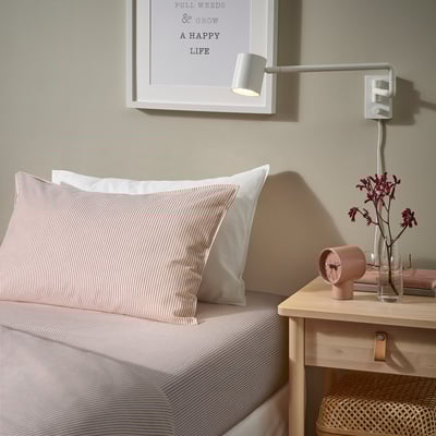 Cama con sabas SOLFIBBLA a raias brancas-vermellas, almofadas brancas, luz de parede, flores e mesa de noite de madeira.