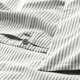 Camisa de raias gris con botón medio desfeito, mostrando detalles de número de fíos. Primeiro plano da textura e costura do tecido.