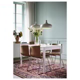 Comedor moderno con mesa branca, cadeiras marróns e luces colgantes. Paredes azuis, alfombra floral, flores sobre a mesa.