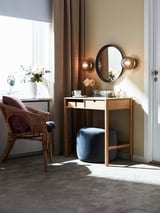 Luxoso dormitorio con cadeira de vimbio, almofadas marróns, vaidade, espello redondo e lámpadas SOLKLINT.