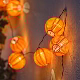 Cadea de luces de lanterna laranxa redondas, perfectas para uso ao aire libre, emitindo un brillo cálido.