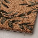 Alfombra con patrón de follas, textura de coir natural, sensación robusta, colocada no chan de madeira.