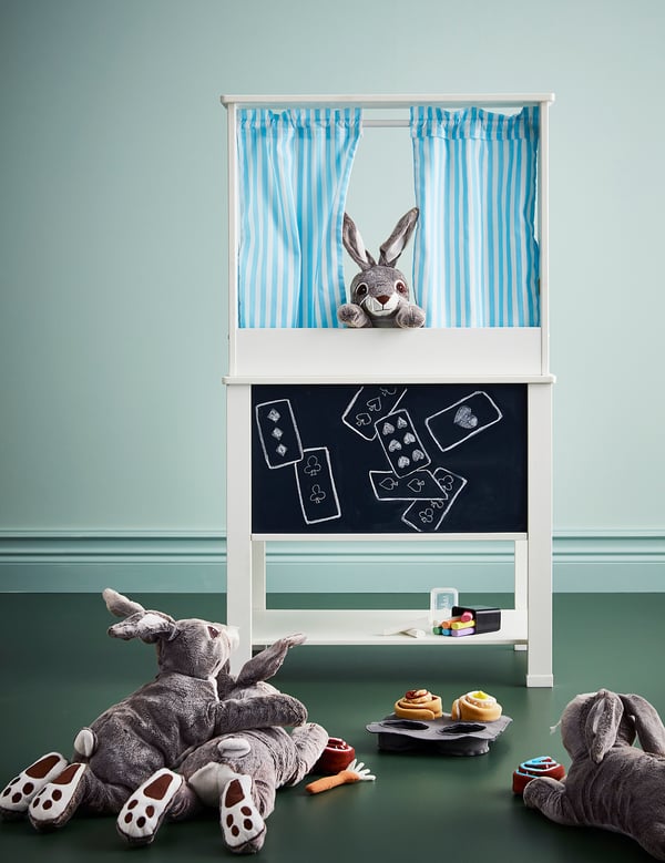 Unha configuración de cociña lúdica con coellos de peluche, cortinas de raias e taboleiro.