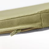 Primeiro plano dun coxín con cremalleira, beige-verde cobre o bordo, mostrando costuras de calidade e tecido resistente.