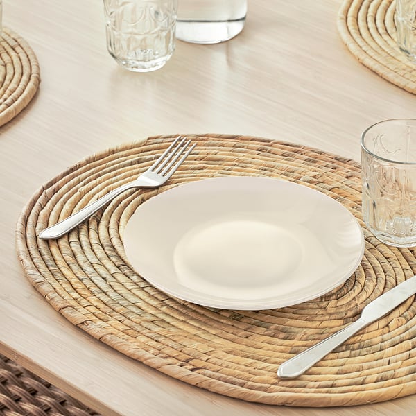 Alfombra natural tecida a man con placa branca, garfo, coitelo e vidro. Forma ovalada, coaster engade instantaneamente textura á mesa.