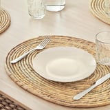 Alfombra natural tecida a man con placa branca, garfo, coitelo e vidro. Forma ovalada, coaster engade instantaneamente textura á mesa.