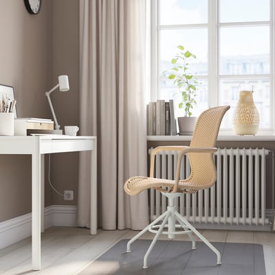 Oficina na casa minimalista con cadeira xiratoria STIGBYGEL, escritorio pequeno, portátil, libros, lámpada, planta e luz natural.