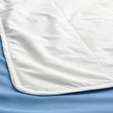 Duvet branco crocante, liso e ben dobrado sobre roupa de cama azul claro.