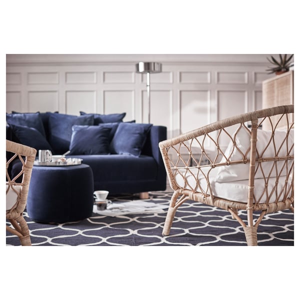 Sala de estar moderna con sofá seccional azul e cadeiras de vimbio sobre alfombra de patróns escuros.