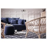 Sala de estar moderna con sofá seccional azul e cadeiras de vimbio sobre alfombra de patróns escuros.