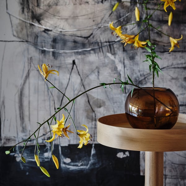 Vaso de vidro marrón sobre soporte de madeira con flores amarelas.