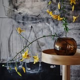 Vaso de vidro marrón sobre soporte de madeira con flores amarelas.